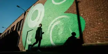 A person walking past a vibrant green and teal urban mural on a weathered brick building, illuminated by a single dramatic light source, symbolizing the integration of art into city spaces.