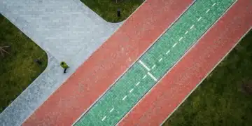 An aerial drone view of a modern urban park where three distinct pathways of stone, brick, and green glass converge, symbolizing the intersection of creativity, culture, and future trends.