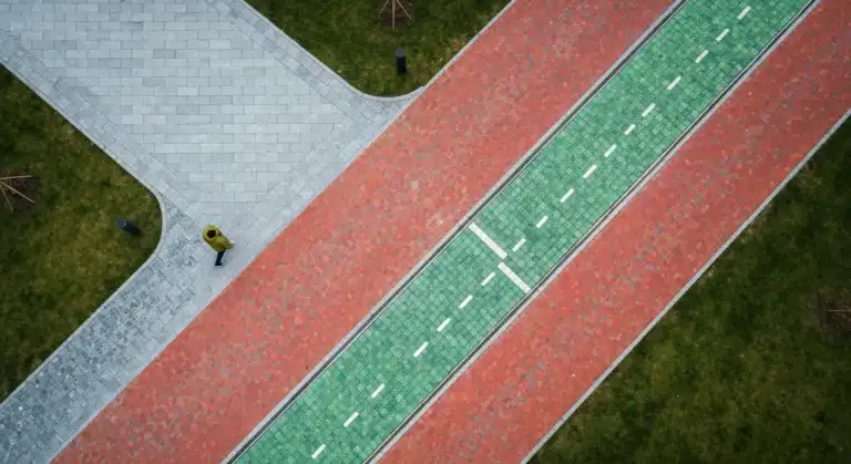 An aerial drone view of a modern urban park where three distinct pathways of stone, brick, and green glass converge, symbolizing the intersection of creativity, culture, and future trends.
