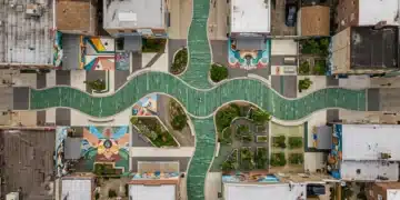 An aerial view of a dynamic urban plaza featuring a flowing green glass pathway, surrounded by geometric public art and community gardens, symbolizing the convergence of creative ideas, cultural insights, and future trends in modern living.