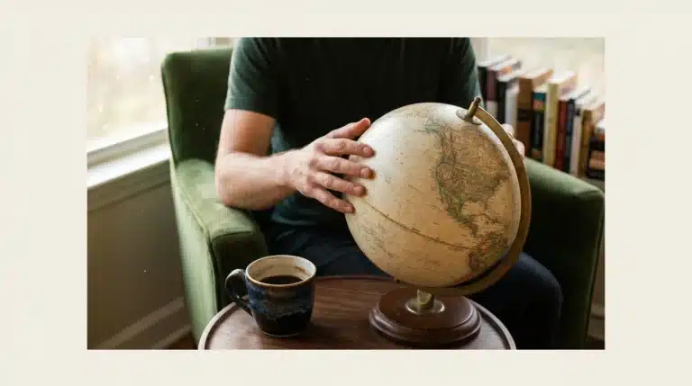 A person tracing lines on a vintage globe, symbolizing the interconnectedness of ideas, culture, and future in modern living, with colorful books in the background.