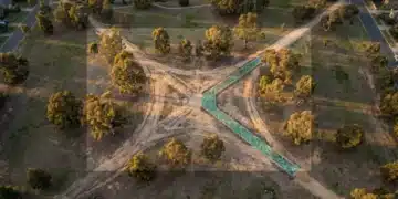 Aerial view of an urban park at golden hour, showing three old, worn dirt paths intertwined, with a new, geometrically patterned path made of iridescent green glass tiles cutting a fresh trajectory through them, symbolizing true innovation versus imitation.